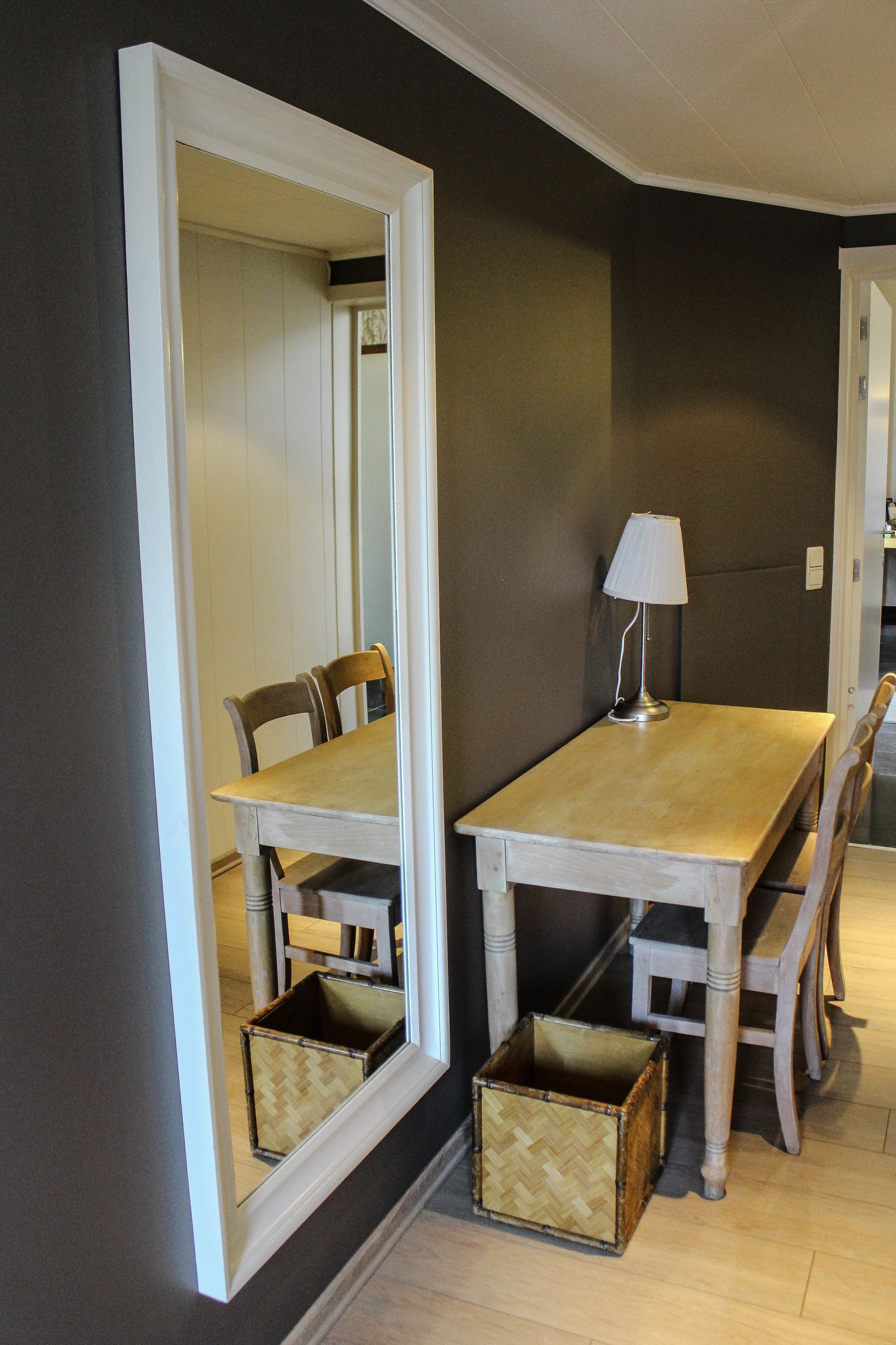 A dining area with a wooden table and chairs, a mirror, a lamp, and two woven baskets.