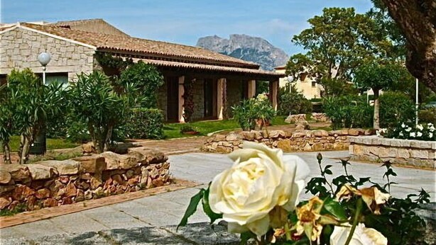 A building with a stone facade and a tiled roof, surrounded by greenery and a stone pathway. - Il Borgo Appartamenti by Kasavacanze (Loiri Porto San Paolo)