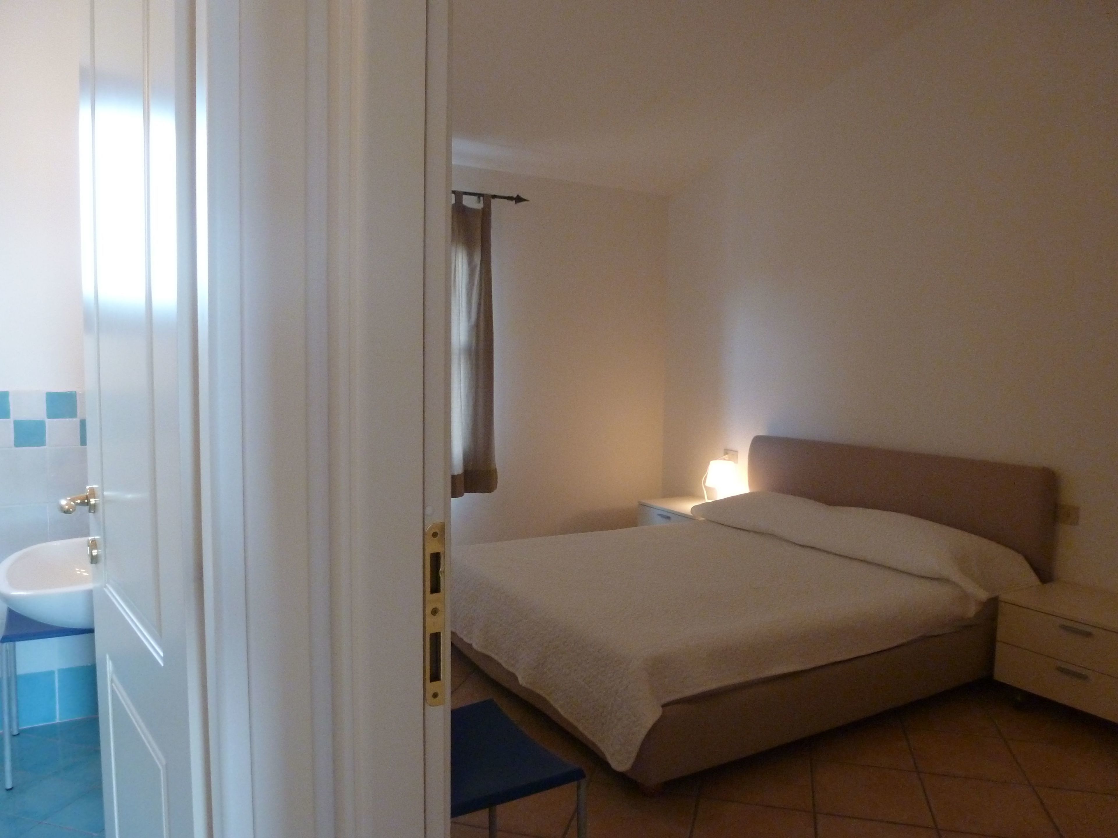 Une chambre à coucher avec un lit, une table de chevet et une petite fenêtre avec des rideaux.