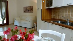 A compact living space with a kitchenette, a white sofa, and a dining area with a table and chairs. - Il Borgo Appartamenti by Kasavacanze (Loiri Porto San Paolo)