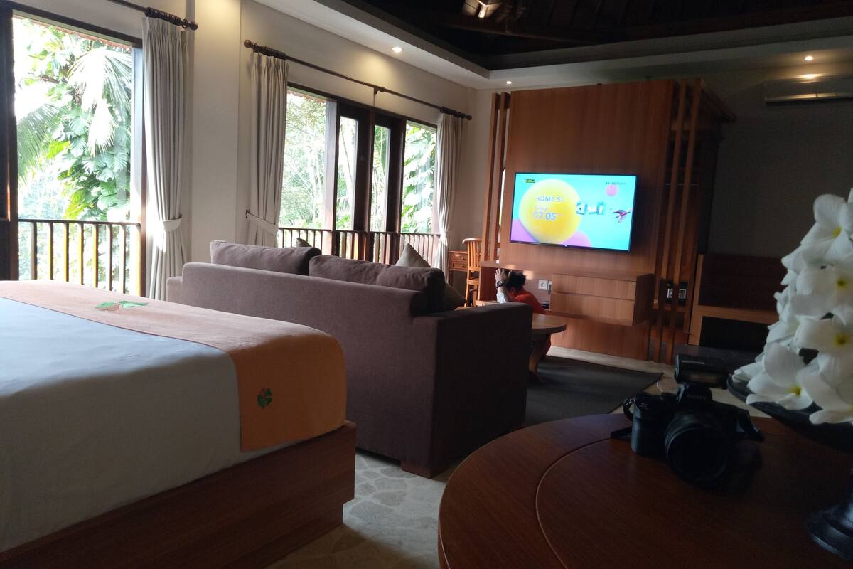 A hotel room with a bed, sofa, TV, and a camera on a table.