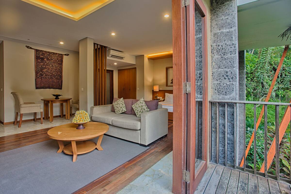 A modern living room with a sofa, coffee table, and chairs, a large window with a view of greenery, and a stone wall.