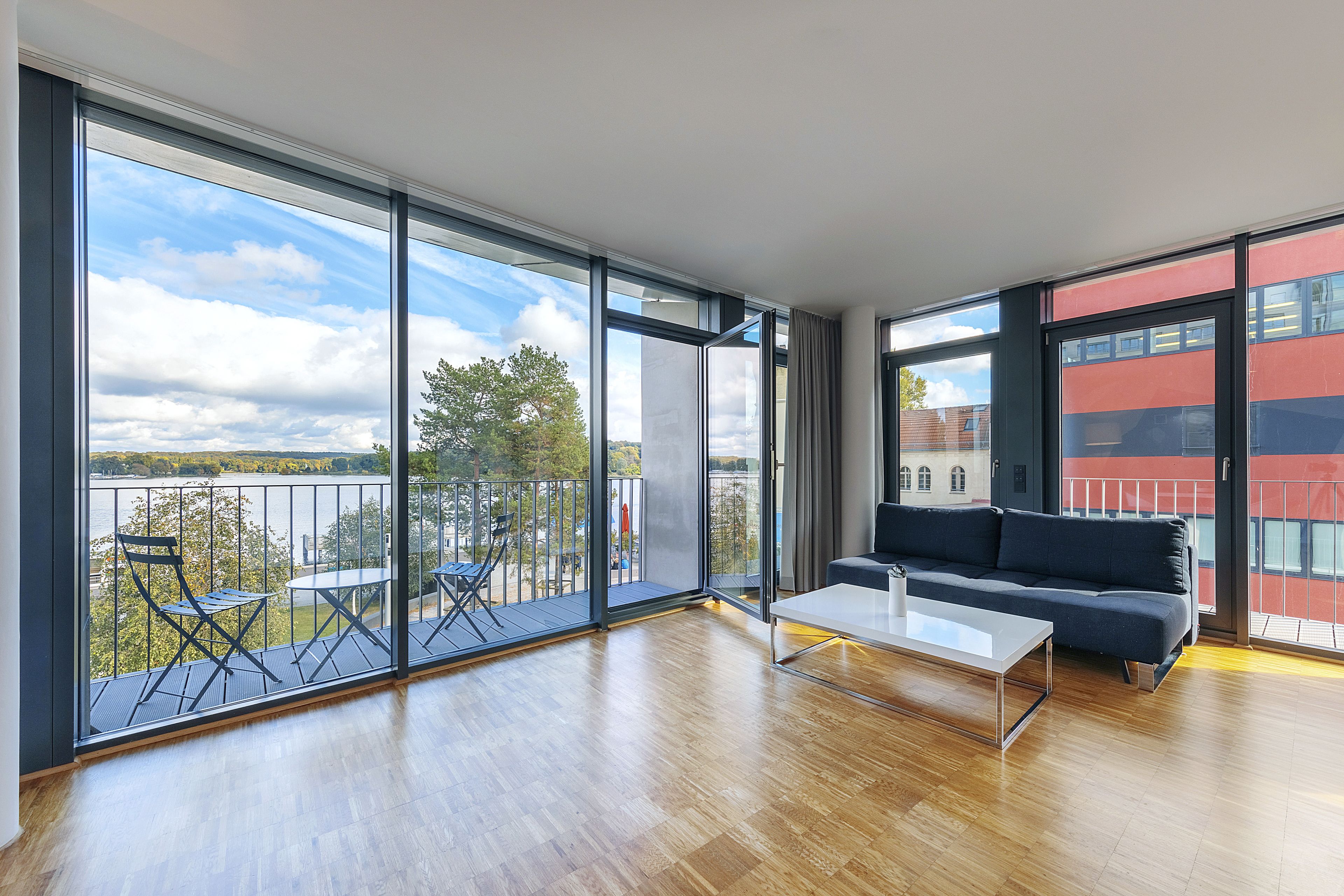 Ein geräumiges Wohnzimmer mit einem großen Schiebeglastür, die auf einen Balkon mit Seeblick und Bäumen führt.