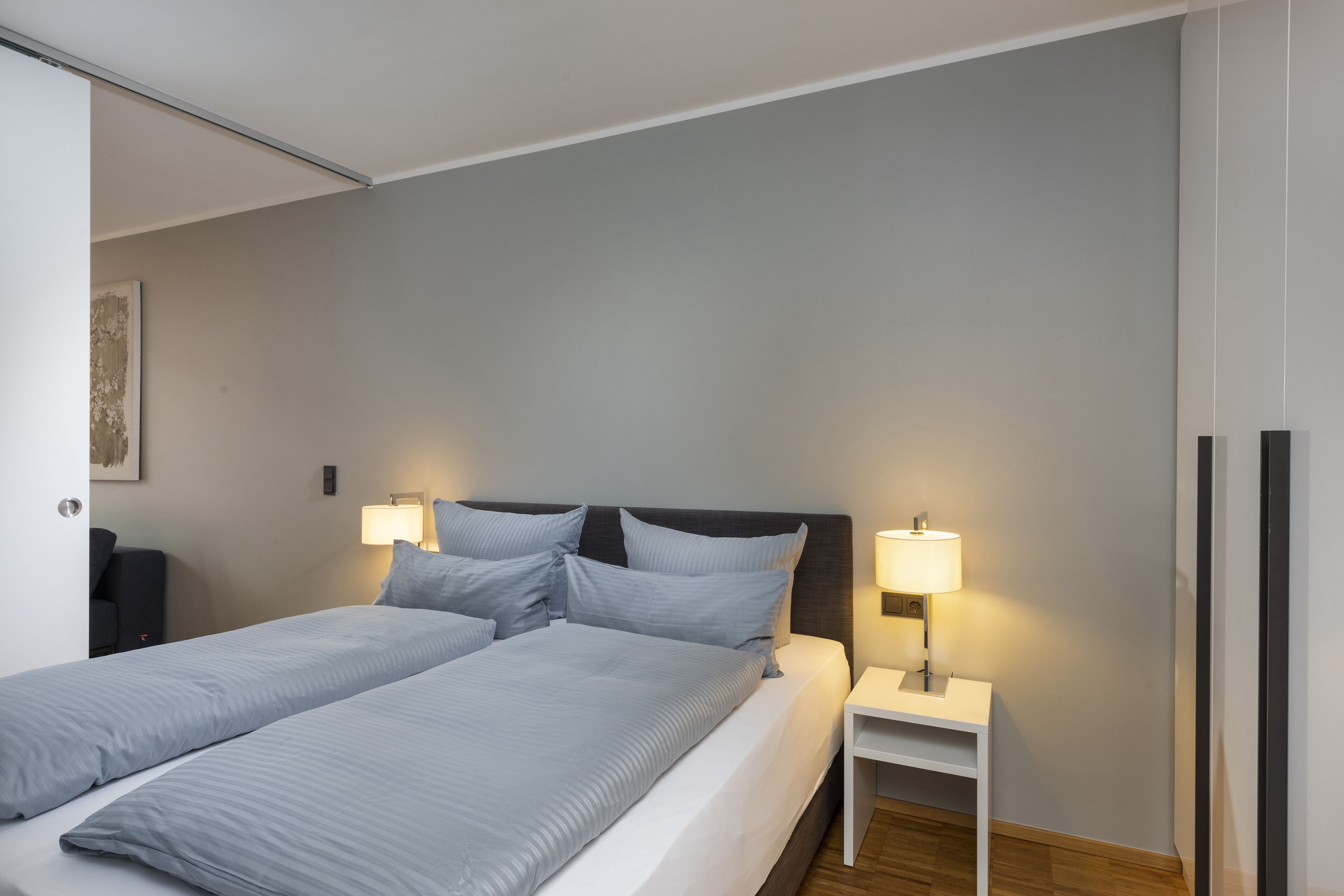 A double bed with a grey headboard and two bedside tables with lamps.