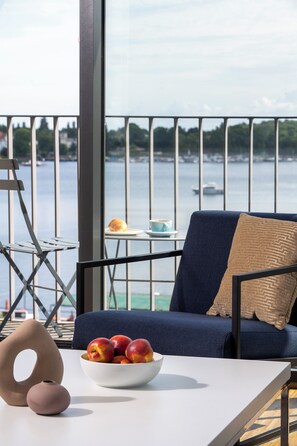 A balcony with a view of the sea, a table with a bowl of fruit, a chair, and a small table with a cup and pastry. - Waveboard Hotel & Boardinghouse  (Potsdam)