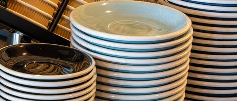 Stacks of plates and cups, a coffee cup with latte art, and a basket of napkins.