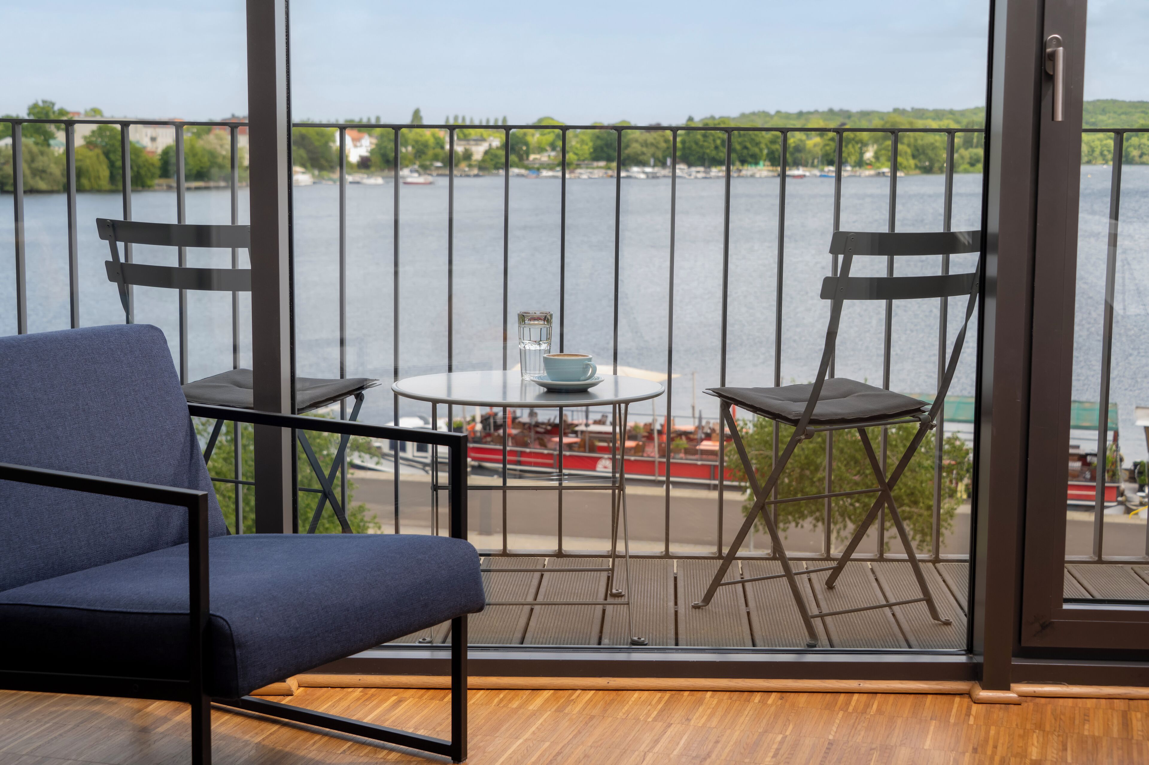 Un balcon donnant sur une rivière, une table avec une tasse et une soucoupe, et deux chaises.