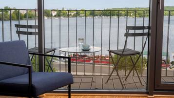 Ein Balkon mit Blick auf einen Fluss, ein Tisch mit Tasse und Untertasse sowie zwei Stühle.