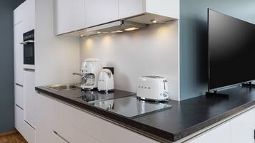 Eine moderne Küche mit weißen Schränken, einer schwarzen Arbeitsplatte, einer Kaffeemaschine, einem Toaster und einem Flachbildfernseher.