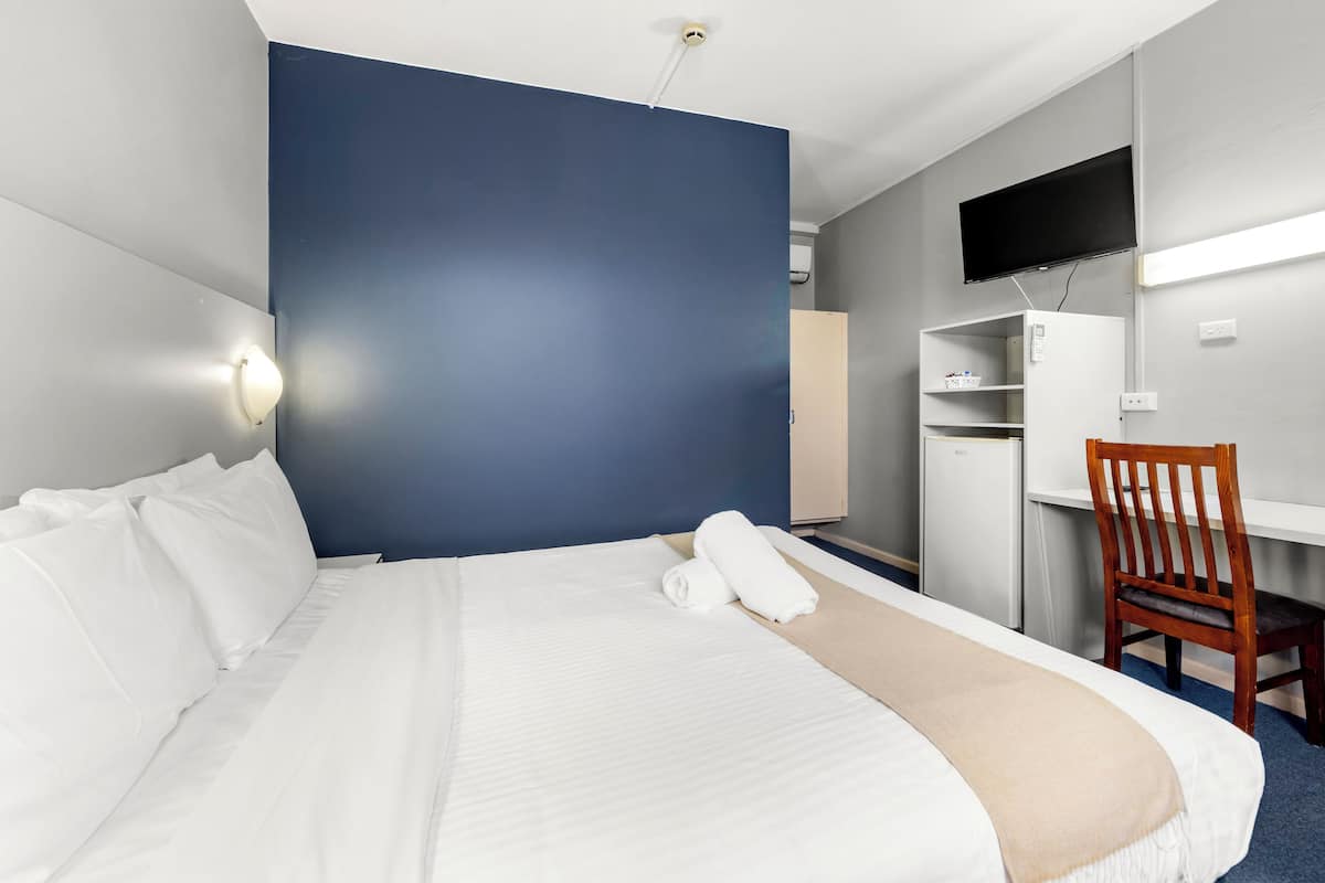 A hotel room with a bed, a desk, a chair, a TV, and a wardrobe.