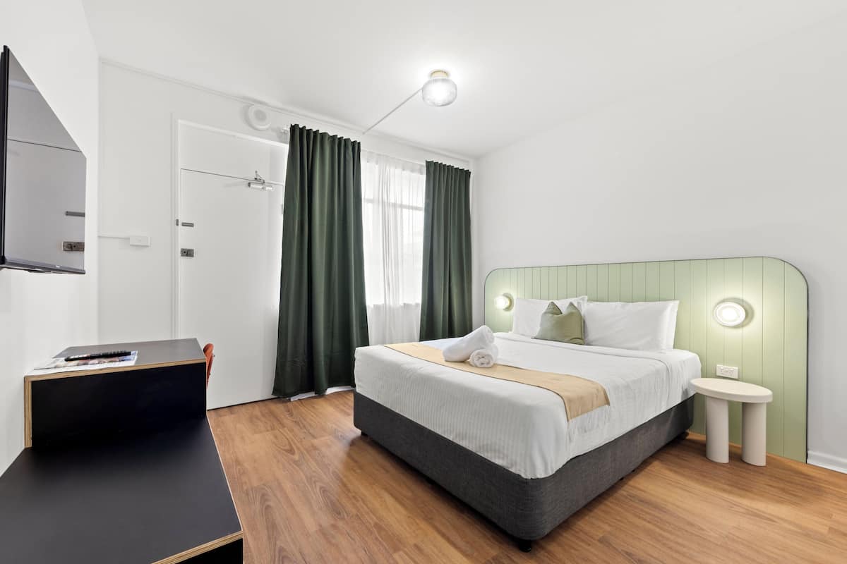 A modern hotel room with a bed, bedside table, and a desk.