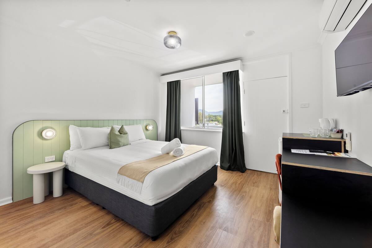 A modern hotel room with a large bed, a desk, a chair, a TV, and a window with curtains.
