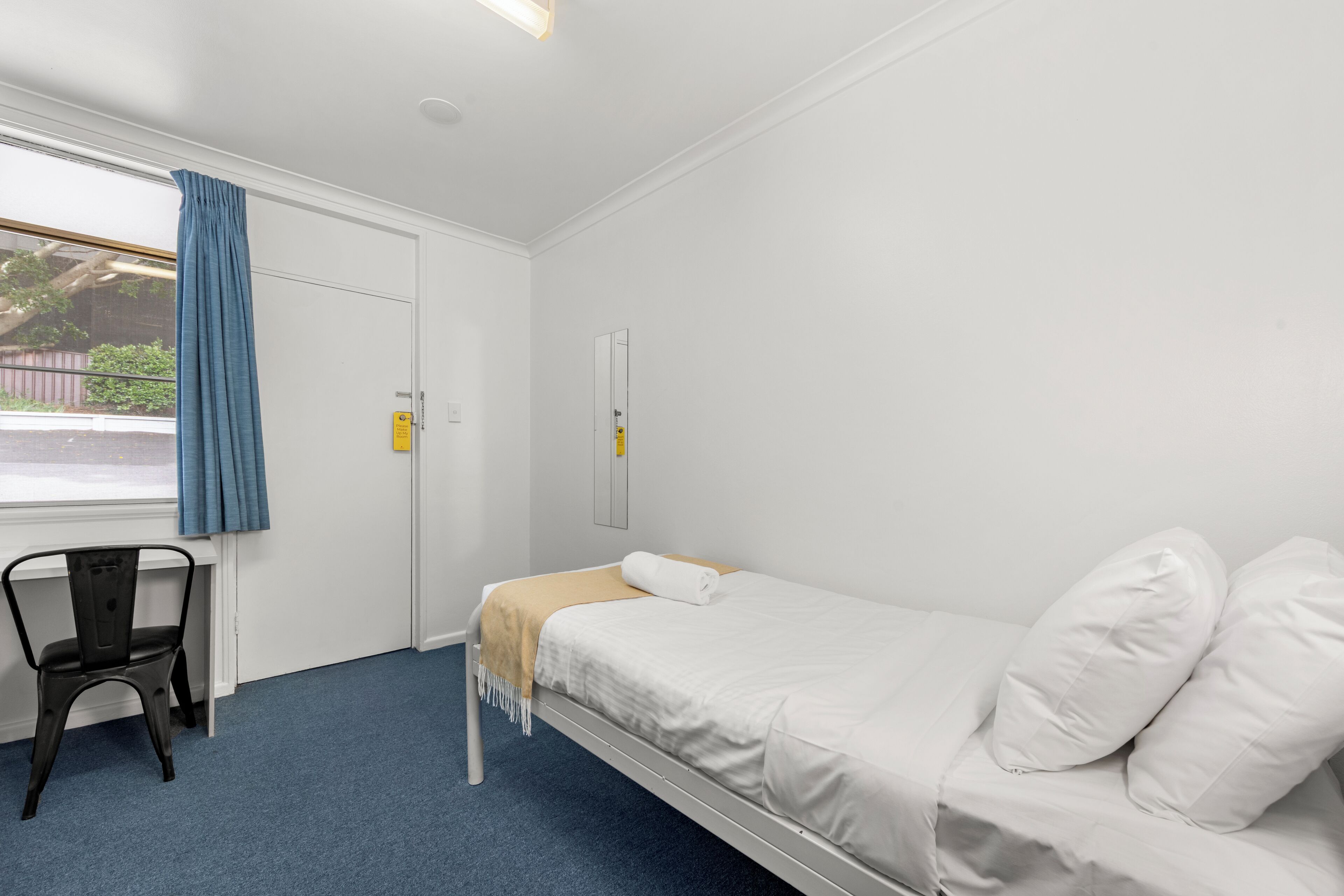 A single-bed room with a window, a chair, and a door.