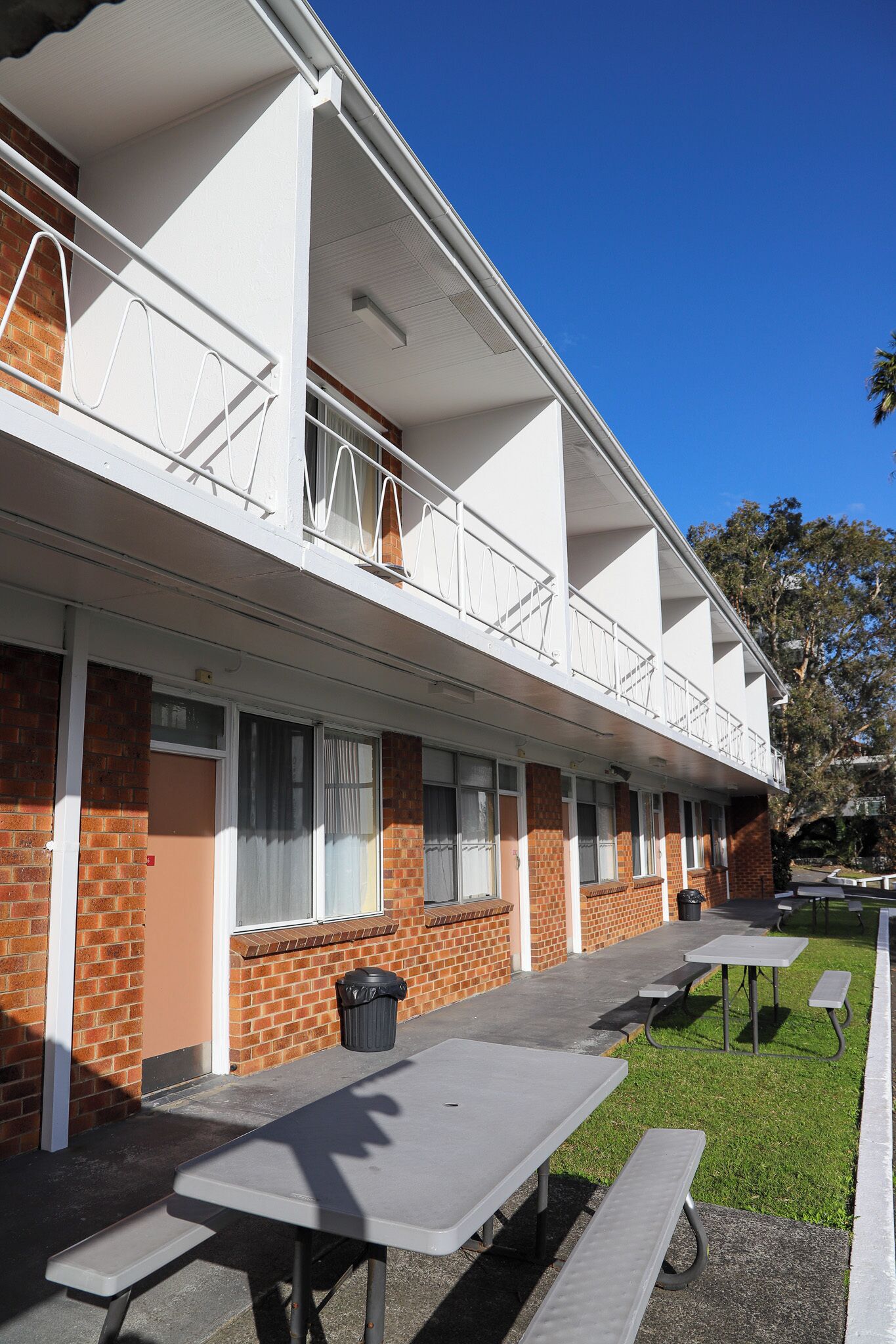 A two-story motel with a balcony, outdoor tables, and a trash bin.