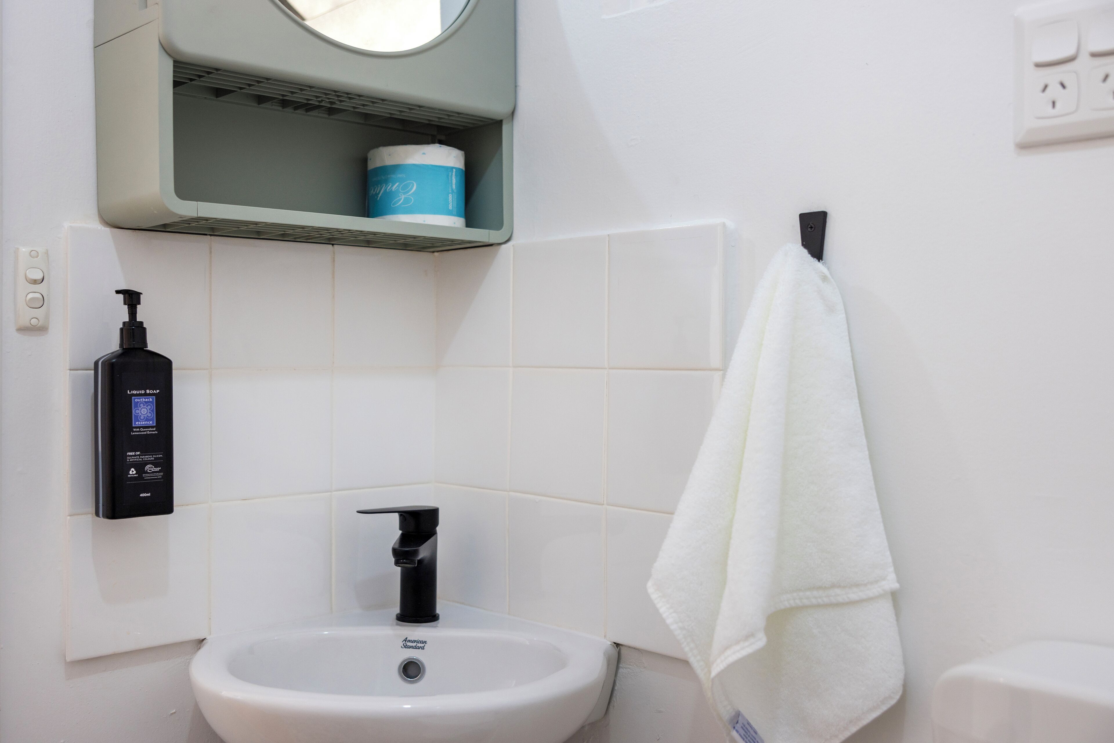 A bathroom with a white sink, a black soap dispenser, a towel hanging on a hook, and a blue container on a shelf.