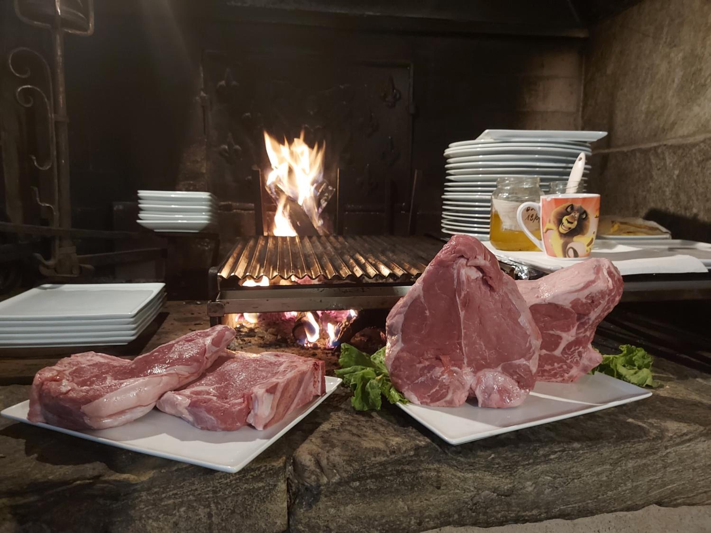 A stone table with raw meat and plates, a grill with flames, and a mug with a cartoon character.