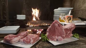 A stone table with raw meat and plates, a grill with flames, and a mug with a cartoon character.