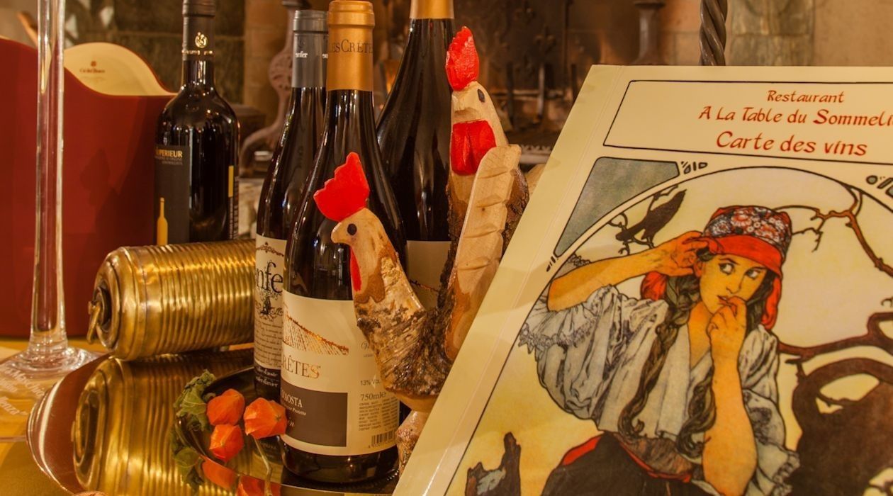 Uma mesa com garrafas de vinho, um menu e galinhas de madeira decorativas.