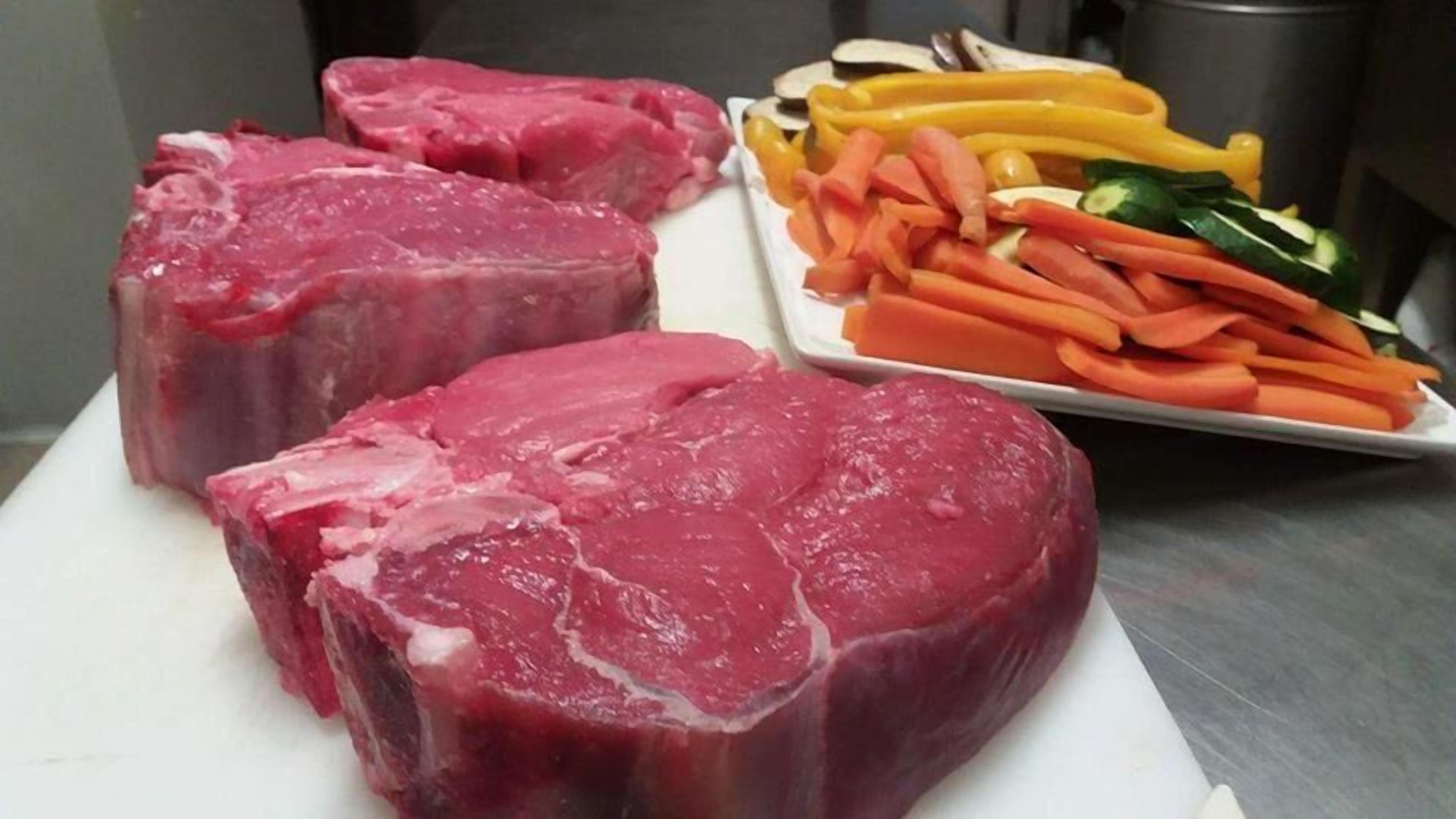 Raw beef and sliced vegetables on a cutting board.
