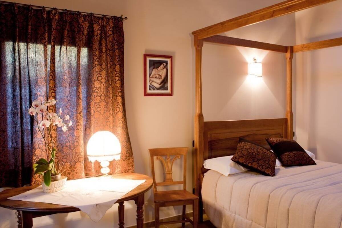A four-poster bed with a wooden headboard, a bedside table with a lamp, and a chair.