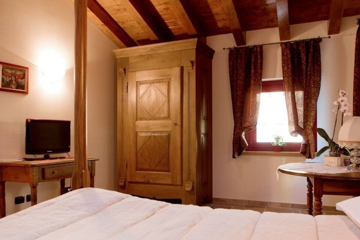 A bedroom with a wooden door, a television on a wooden table, a bedside lamp, and a window with curtains.