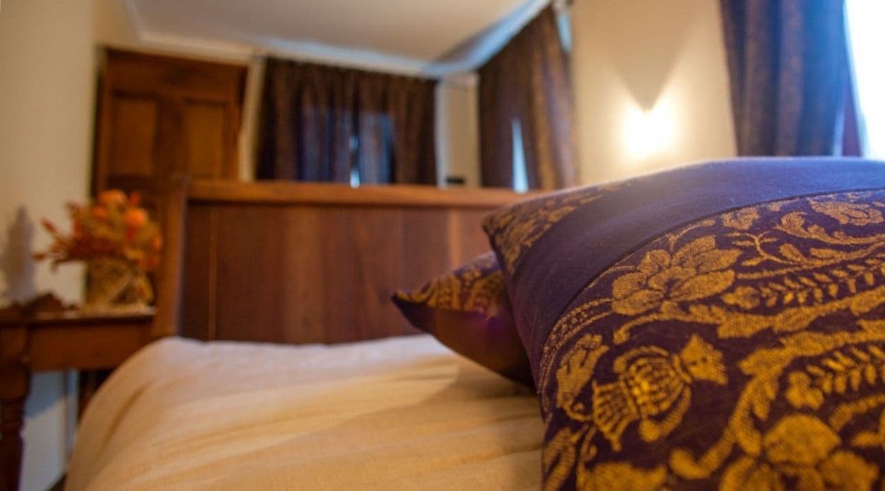 A bedroom with a bed, a wooden headboard, a nightstand with a vase of flowers, and a window with curtains.