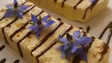 A dessert plate with rectangular pieces of cake, drizzled with chocolate sauce and garnished with blue flowers and a strawberry.