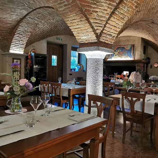 A restaurant with wooden tables and chairs, a stone ceiling, and a fireplace. - A' la Table du Sommelier (Saint-Vincent)