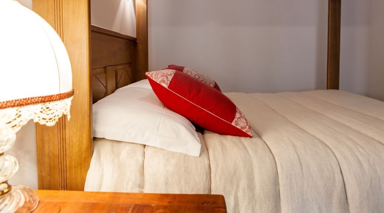 A neatly made bed with a white and red pillow, a wooden headboard, and a bedside table with a lamp.