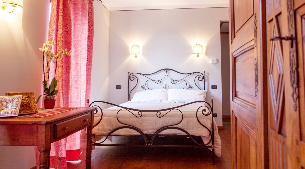 Een slaapkamer met een metalen bedframe, een nachtkastje, een potplant en twee wandlampen.