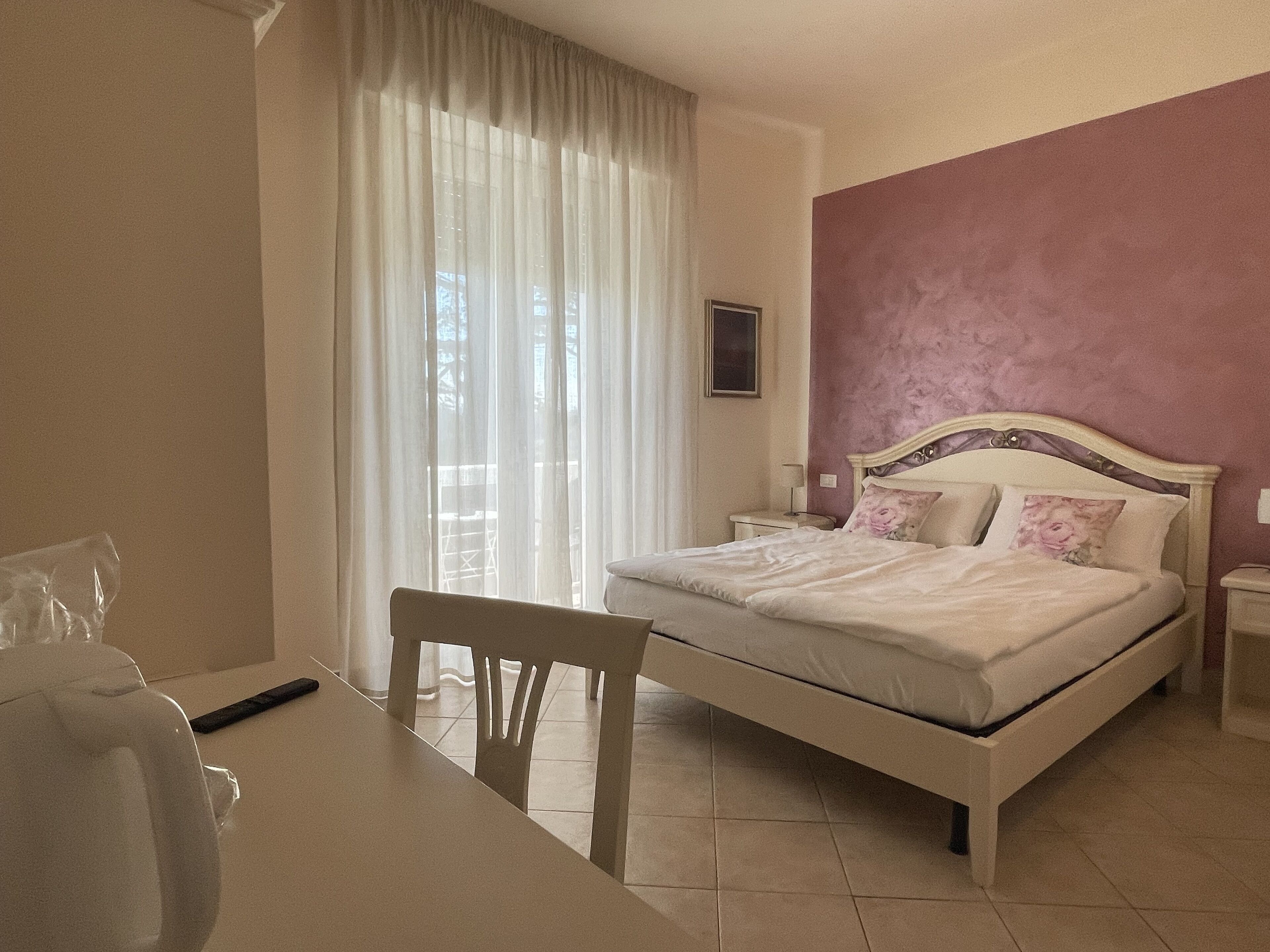 A bedroom with a bed, a chair, a table, and a window with curtains.
