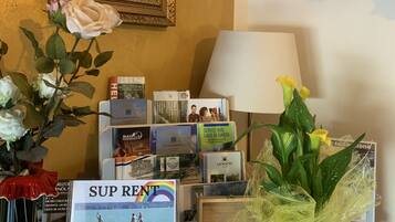 Ein Schreibtisch mit einem gerahmten Gemälde, einer Uhr, einer Vase mit Blumen, einer Lampe, einem Schild und einer Schachtel Pralinen.