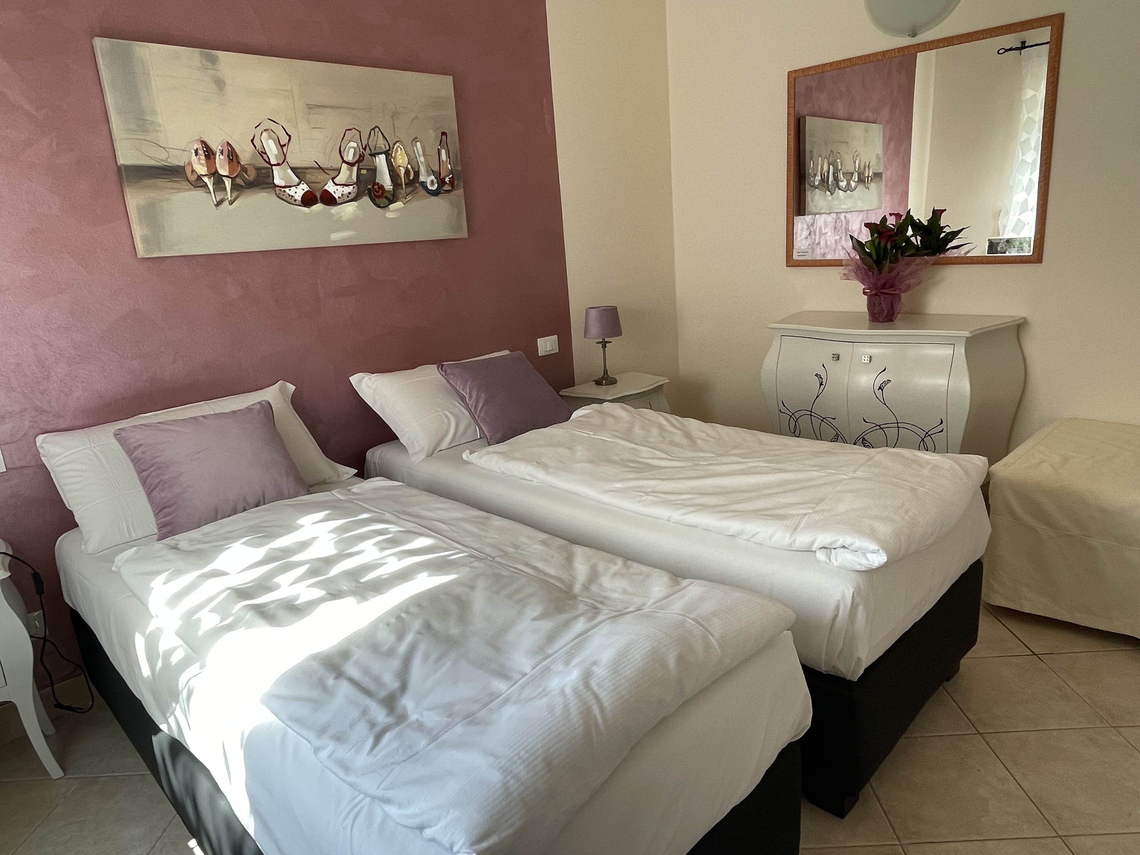 Una habitación de hotel con dos camas, una mesita de noche, un aparador, un espejo y un cuadro en la pared.