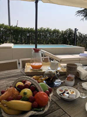 Ein Essbereich am Pool mit Korbmöbeln, einer Obstschale und einem Tisch, gedeckt mit Tellern, Tassen und einer Karaffe.