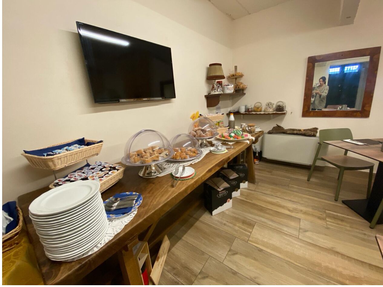 A buffet setup with various food items and plates, a television mounted on the wall, and a mirror reflecting part of the room.