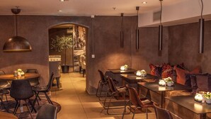 A modern dining area with a mix of round and rectangular tables, accompanied by chairs. There are pendant lights above the tables, and a large mirror on the wall. - Saga Apartments Oslo (Oslo)