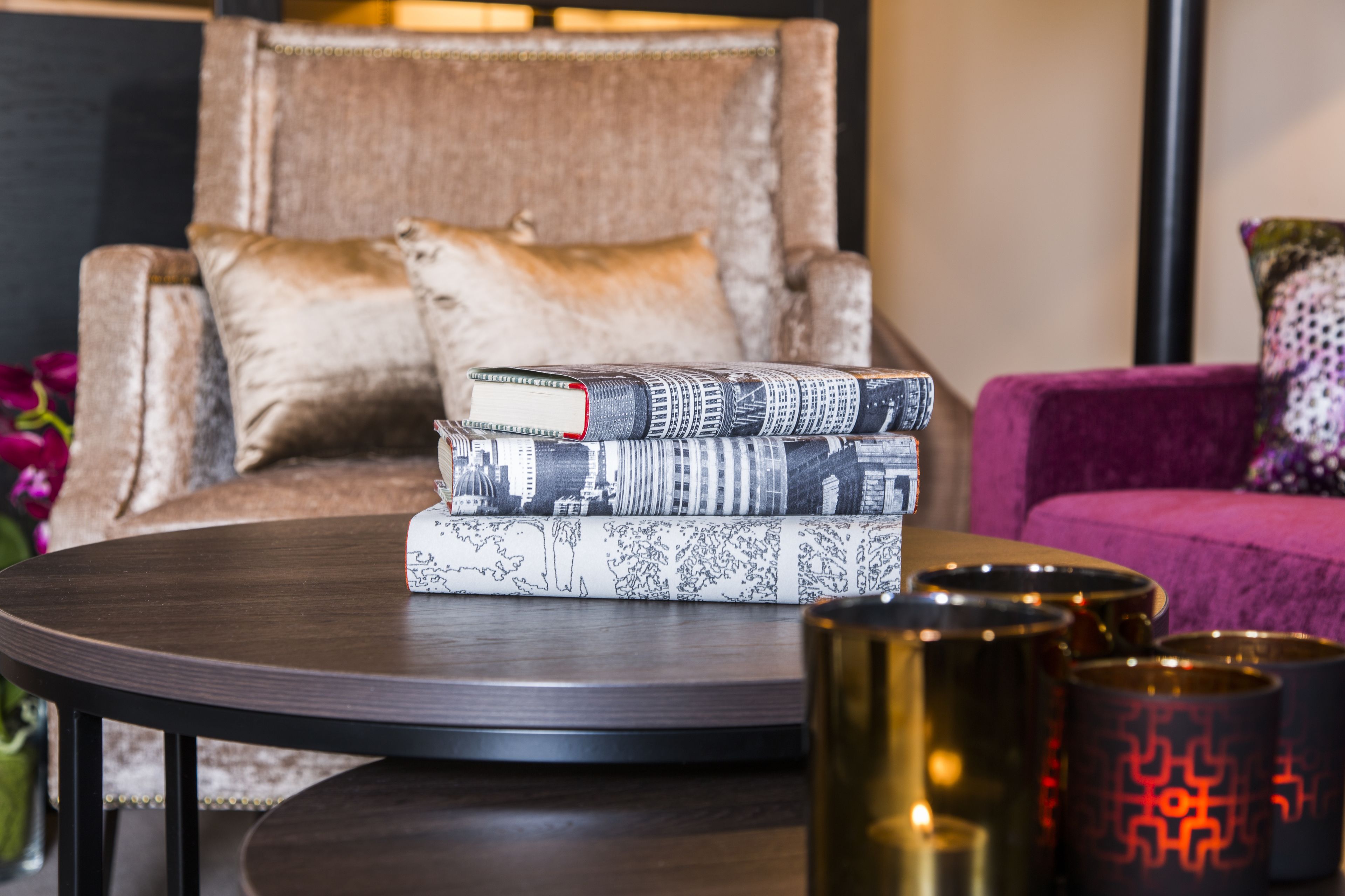 A round table with a stack of books and three metallic candle holders.