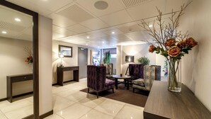 A hotel lobby with a reception desk, seating area, and a decorative vase with flowers. - Saga Apartments Oslo (Oslo)