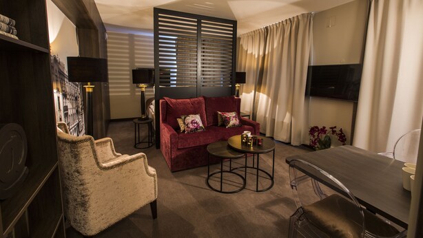 A hotel room with a red sofa, a beige armchair, a small round table, and a TV on the wall. - Saga Apartments Oslo (Oslo)