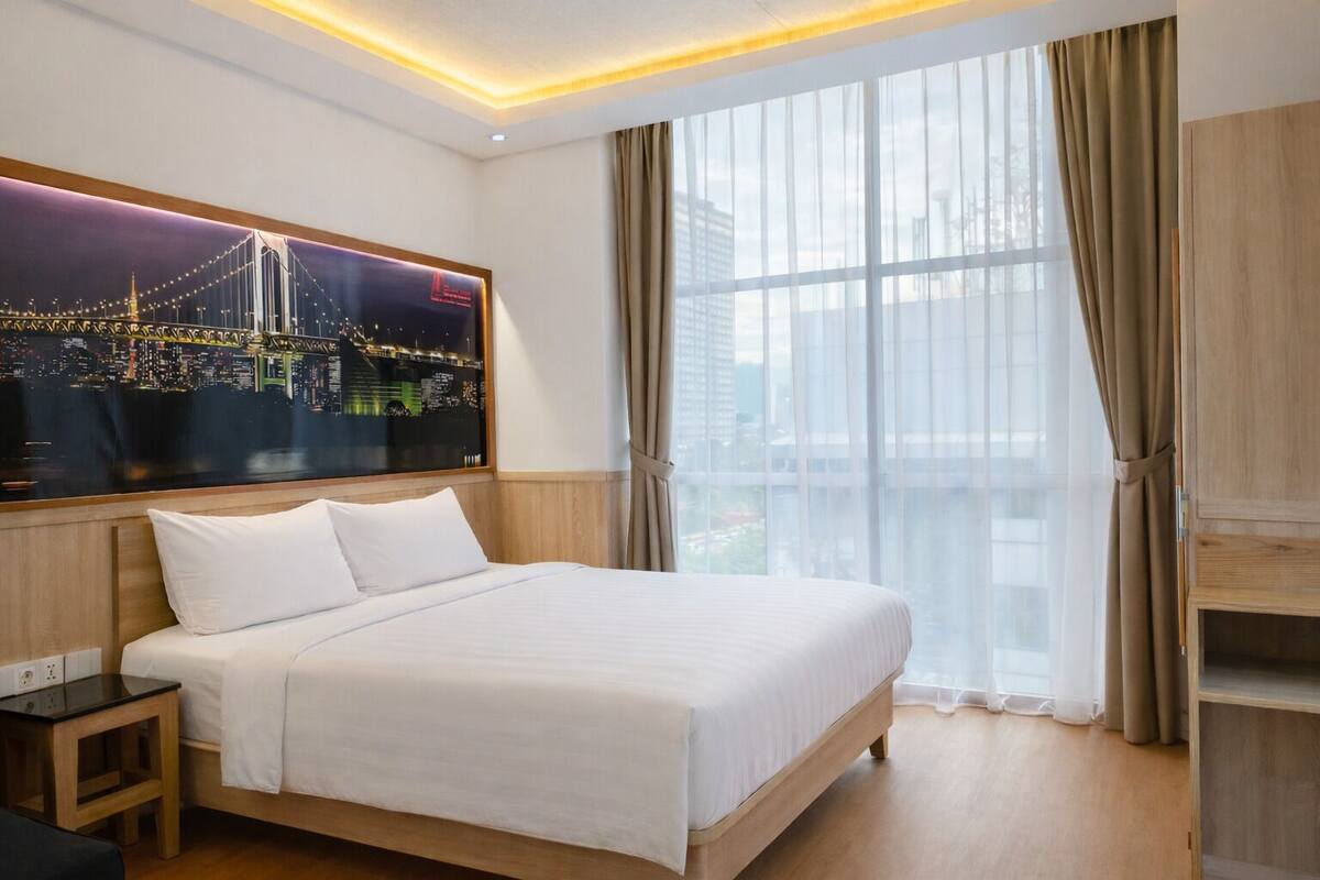 A hotel room with a large bed, a night cityscape poster, a window with curtains, and a wooden cabinet.