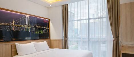 A hotel room with a large bed, a night cityscape poster, a window with curtains, and a wooden cabinet.