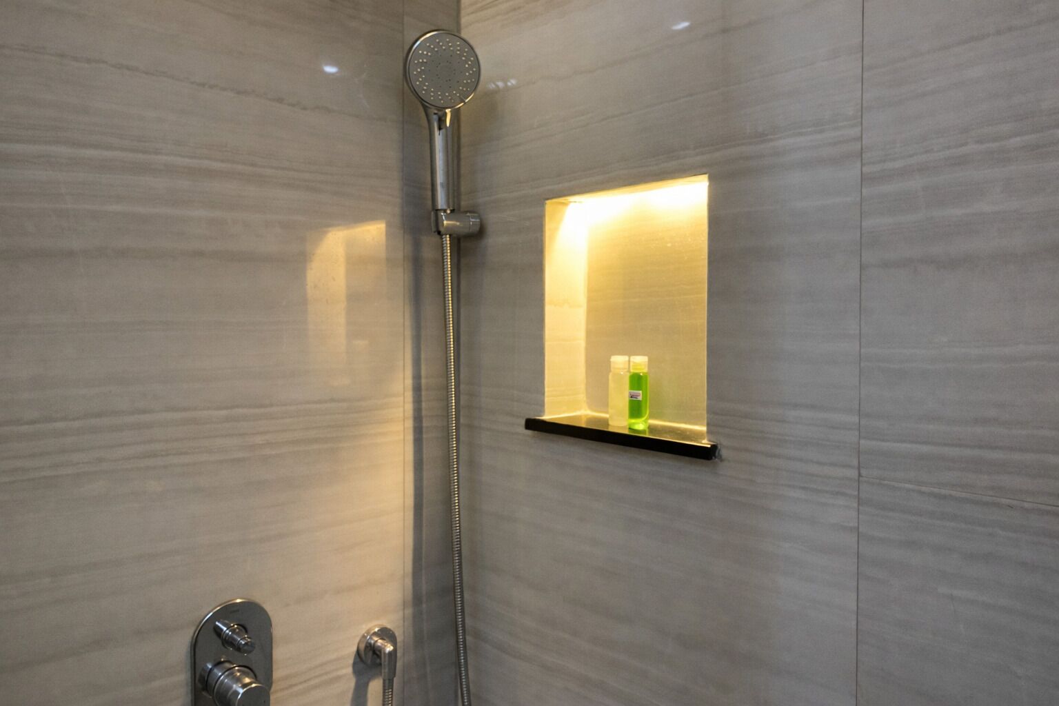 Ein modernes Badezimmer mit Dusche, einer eingebauten Ablage für Toilettenartikel und einem wandmontierten Wasserhahn.
