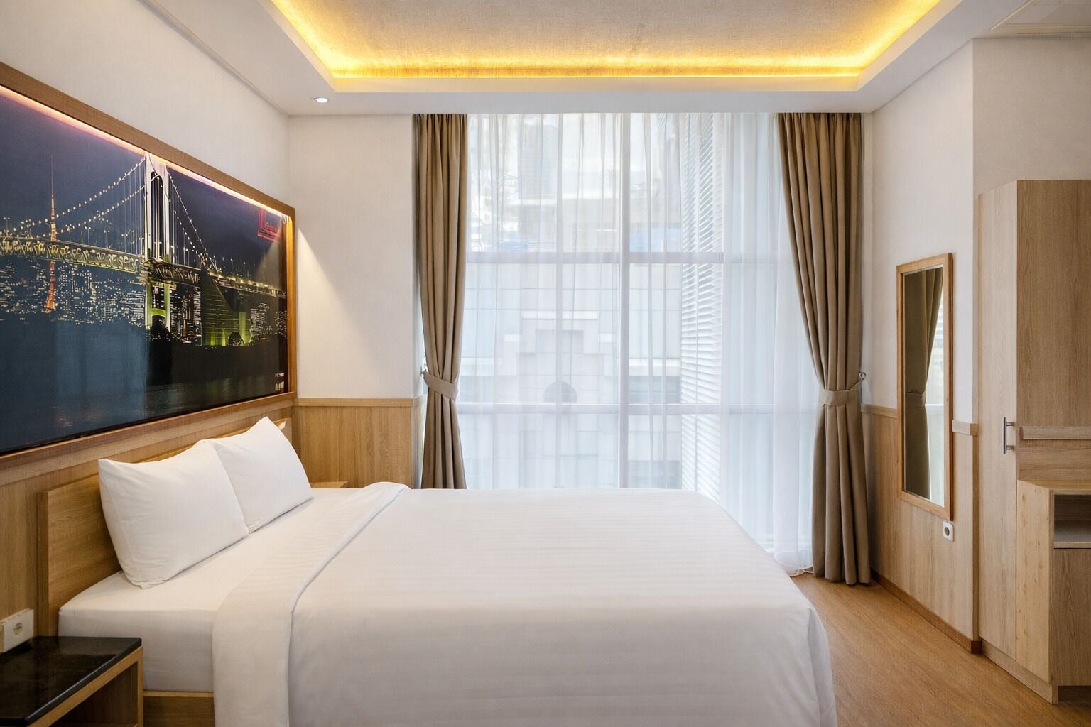 Une chambre d’hôtel avec un grand lit, une table de chevet, une armoire en bois et un tableau représentant un paysage urbain accroché au mur.