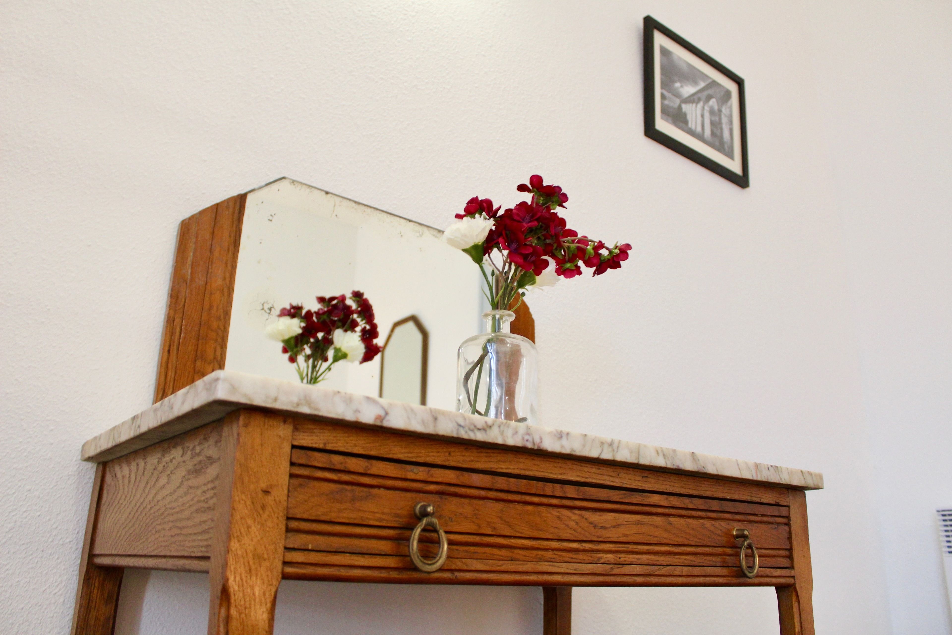 Un tocador de madera con encimera de mármol, un florero con flores y un cuadro en la pared.