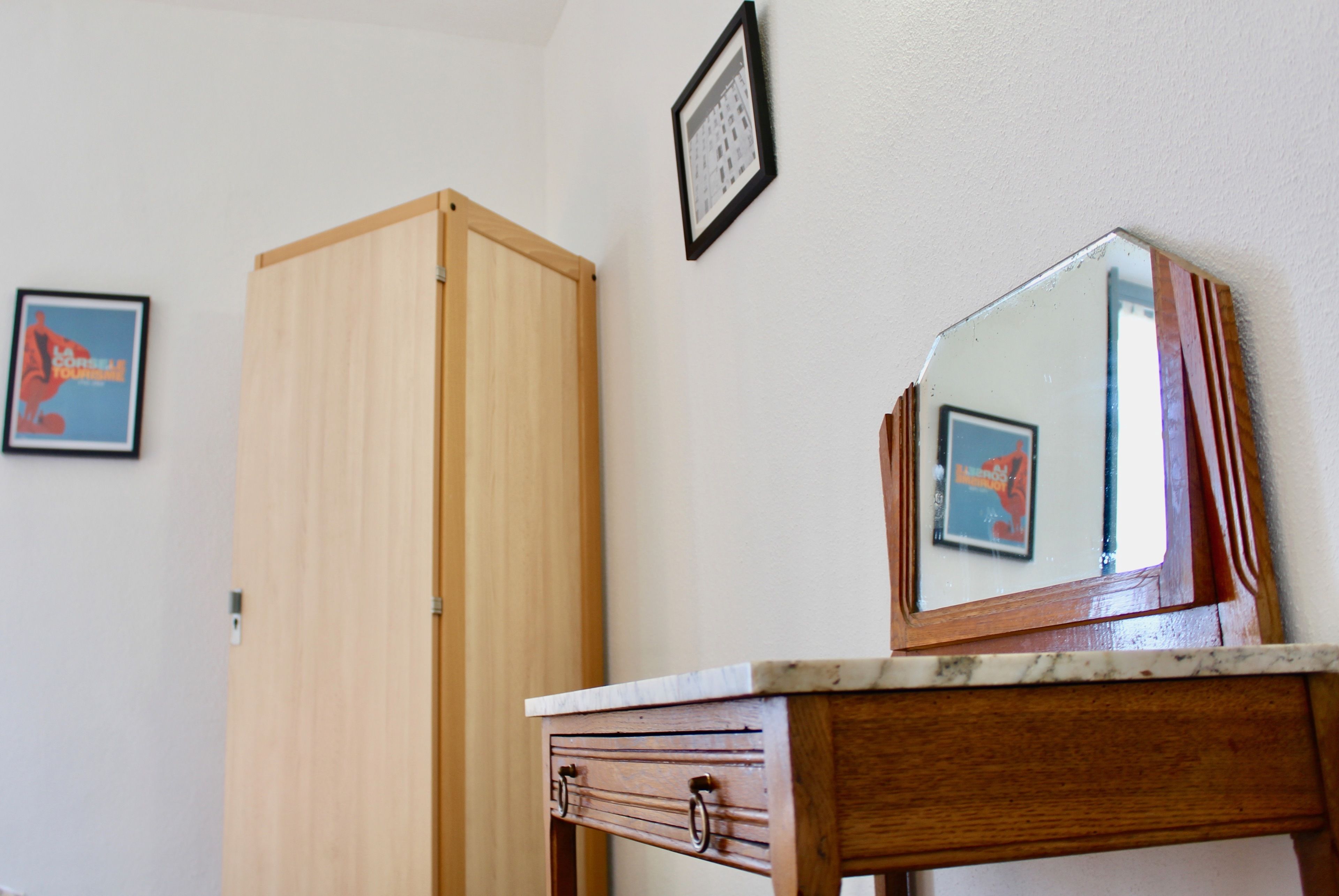 Une pièce avec une armoire en bois, un miroir posé sur une table en marbre et deux tableaux encadrés accrochés au mur.