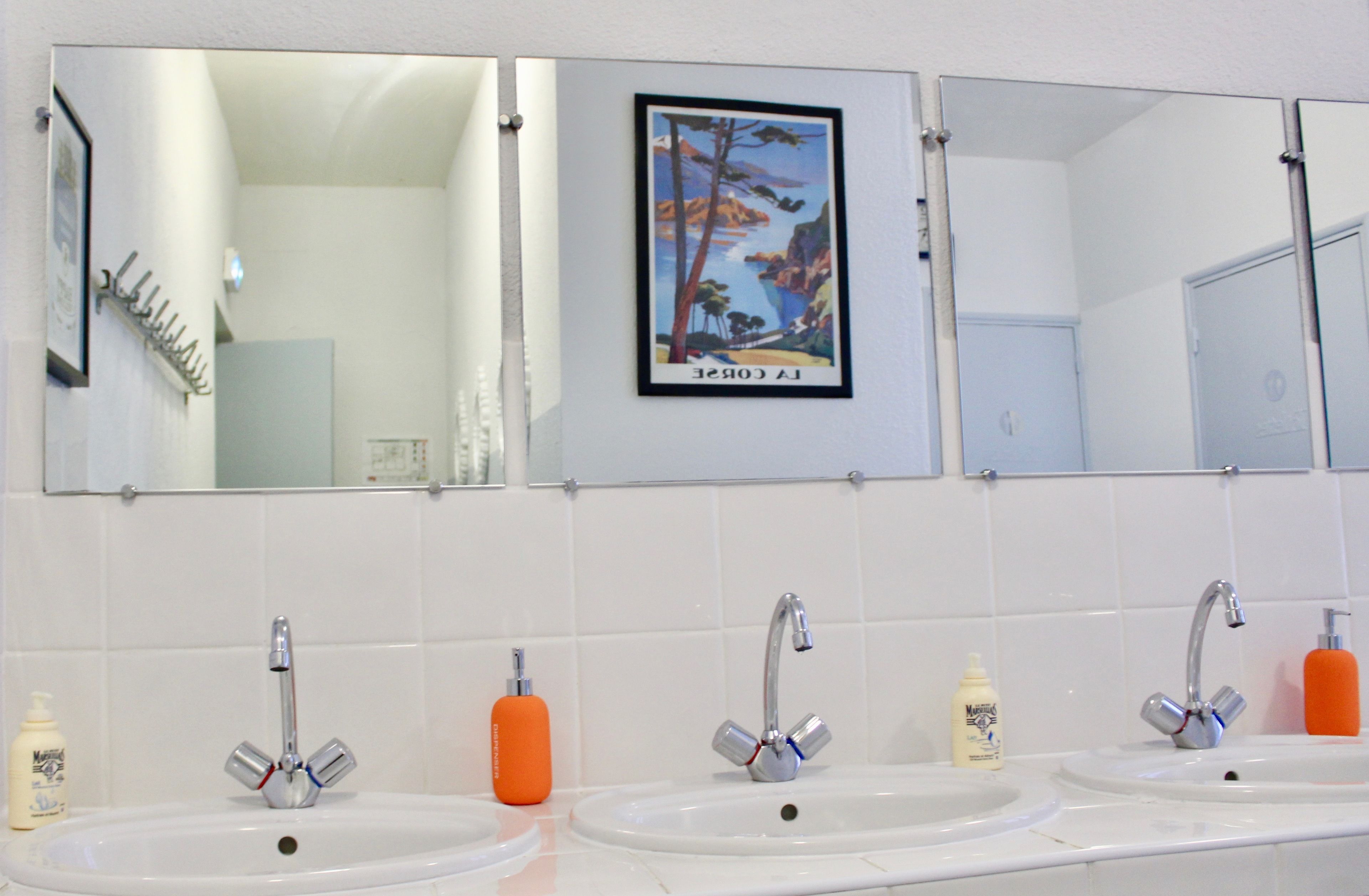Un baño con tres lavamanos, cada uno con un espejo encima. Hay artículos de aseo en la encimera.