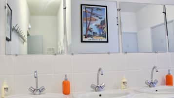 Un baño con tres lavamanos, cada uno con un espejo encima. Hay artículos de aseo en la encimera.
