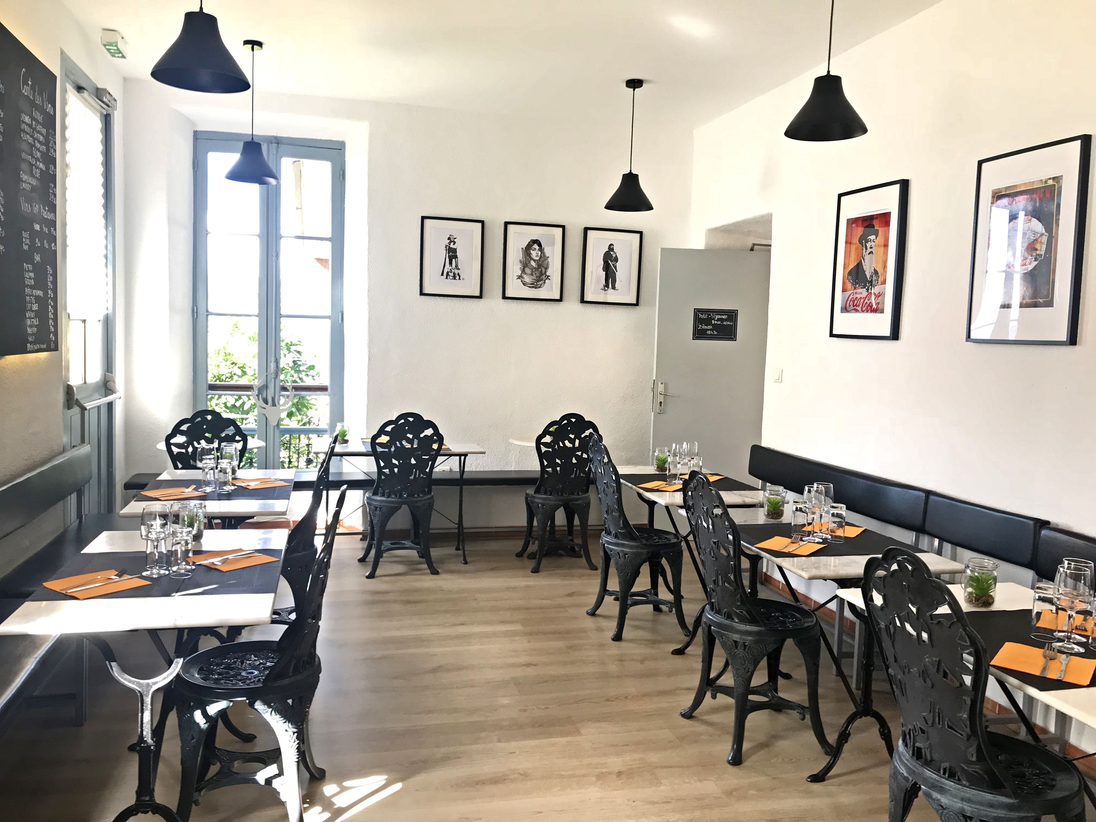 A restaurant interior with wooden flooring, black metal chairs, and tables set for dining.