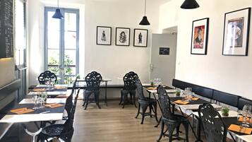 A restaurant interior with wooden flooring, black metal chairs, and tables set for dining.
