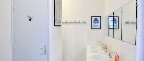 A bathroom with a white door, a hand sanitizer dispenser, and a mirror above two sinks.